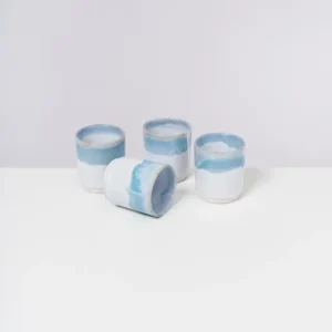 Vier weiße Keramiktassen mit blauen Rändern auf einer weißen Oberfläche, eine liegt umgekippt.