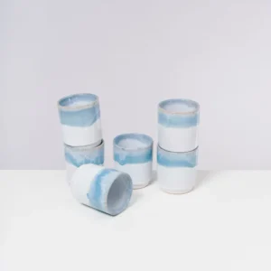 Sechs stapelbare, weiß-blaue Keramiktassen auf einem weißen Tisch vor einem grauen Hintergrund.