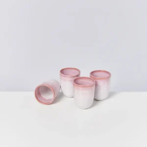 Vier weiße Keramikbecher mit rosa Rand auf weißem Hintergrund, einer liegt seitlich.